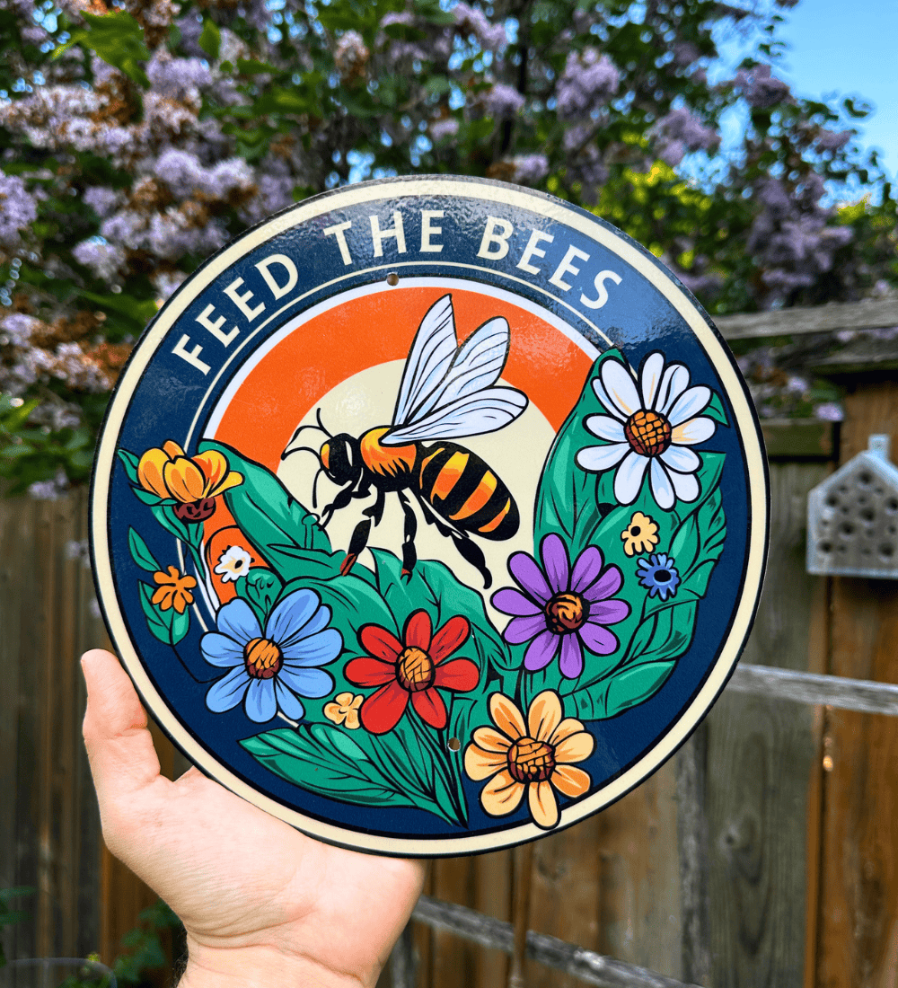 Feed the Bees hand-illustrated garden sign displayed among red zinnias
